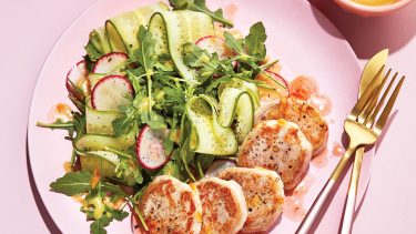 Pink plate topped with pork medallions and salad.