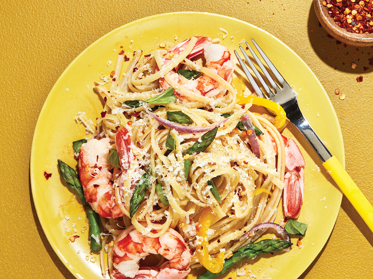 Pasta with shrimp and asparagus on yellow plate.