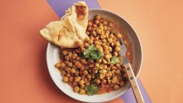 Bowl of chana masala with naan on purple and orange background.