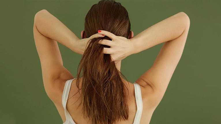 Women on green background applying hair oil through her hair.