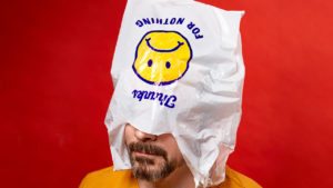 A man with a beard and yellow shirt with a plastic bag over his head that reads "Thanks for nothing," along with a sad face emoji