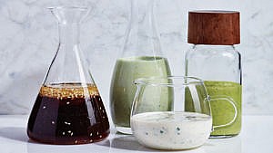 Clear jars filled with different homemade dressings in front of a light-coloured marble background.