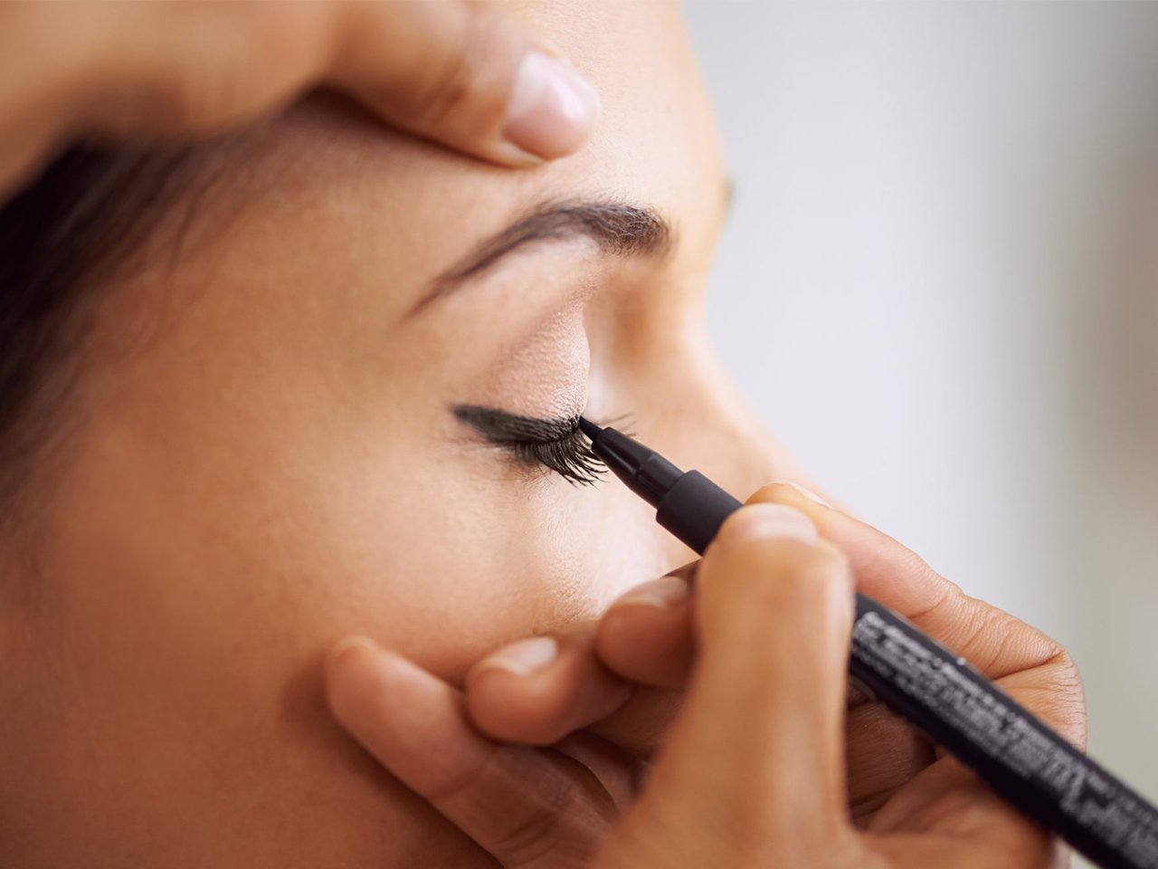 A woman applies liquid eyeliner to an eyelid for a piece on how to apply liquid eyeliner.