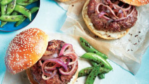 Caramelized onions on burgers with grilled sugar snap peas on parchment paper.