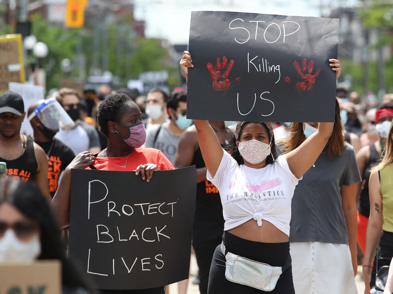 A photo of an anti-racism march in Toronto on June 6, 2020, with a Black woman holding a sign that says "Stop Killing Us." 