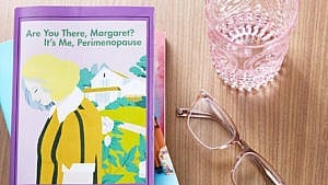 Overhead shot of a stack of books, glasses, and an empty glass of water. Top book on stack says "Are you there, Margaret? It's me, Perimenopause" and shows a blonde woman hanging her head