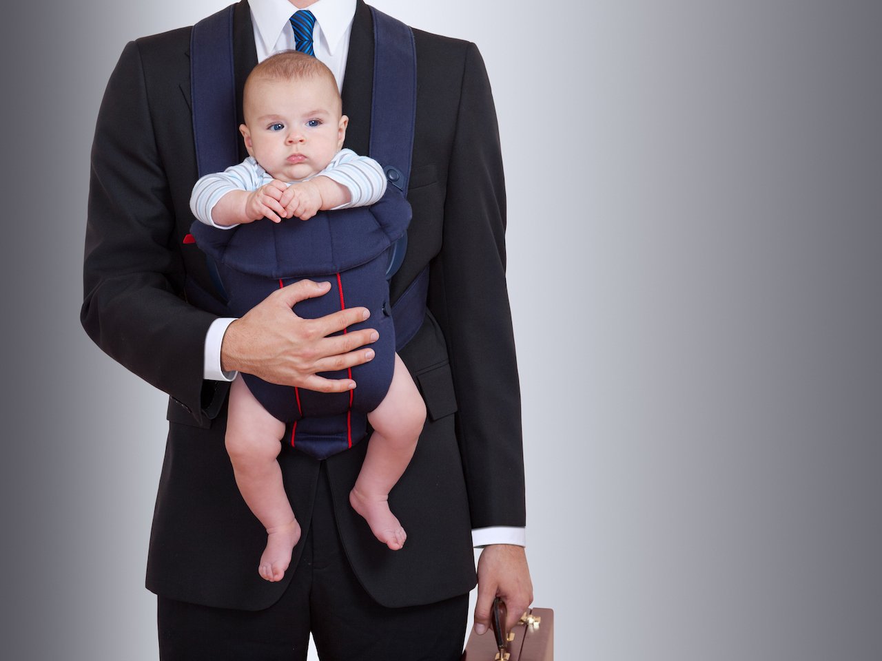Image of a man in a suit holding a baby in a carrier, with the man's head missing