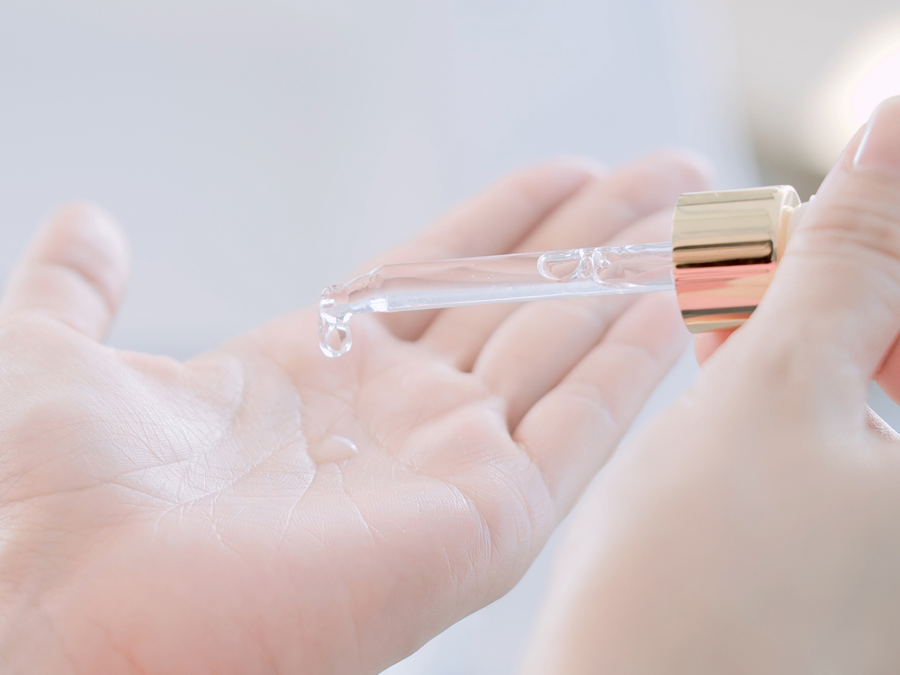 A woman using a pipette to drop serum into her palm for an article on exfoliating skincare acids like AHAs and BHAs, including glycolic, lactic and salicylic acids.