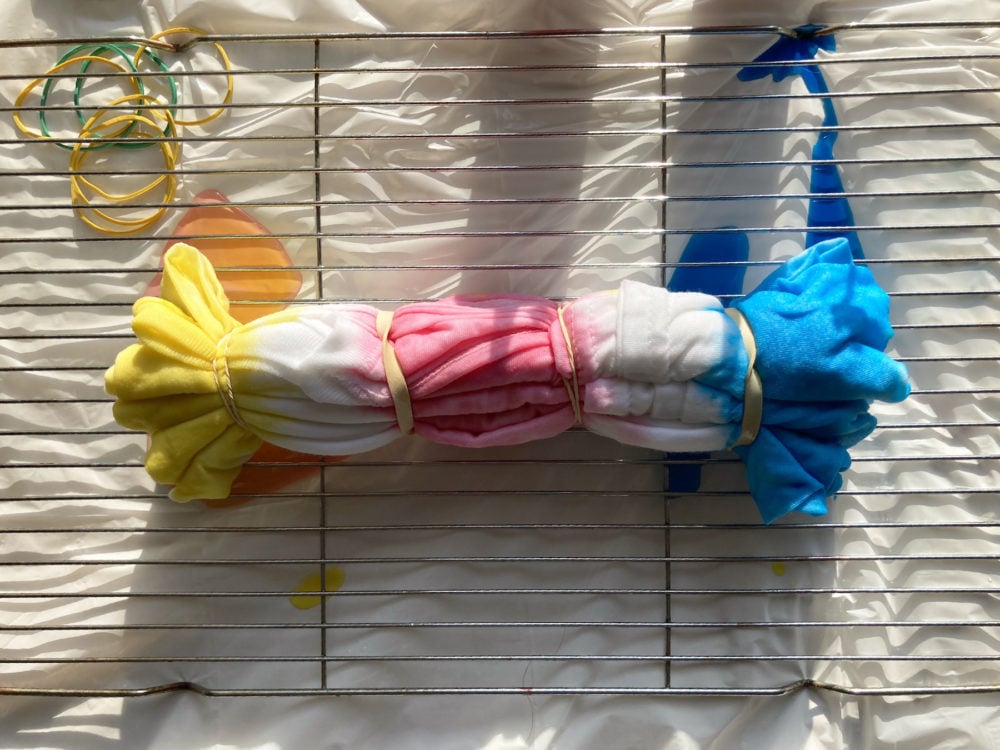A t-shirt in the process of being tie-dyed yellow, pink and blue