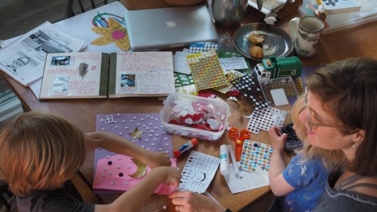 a woman and two toddlers sit at a table filled with craft supplies