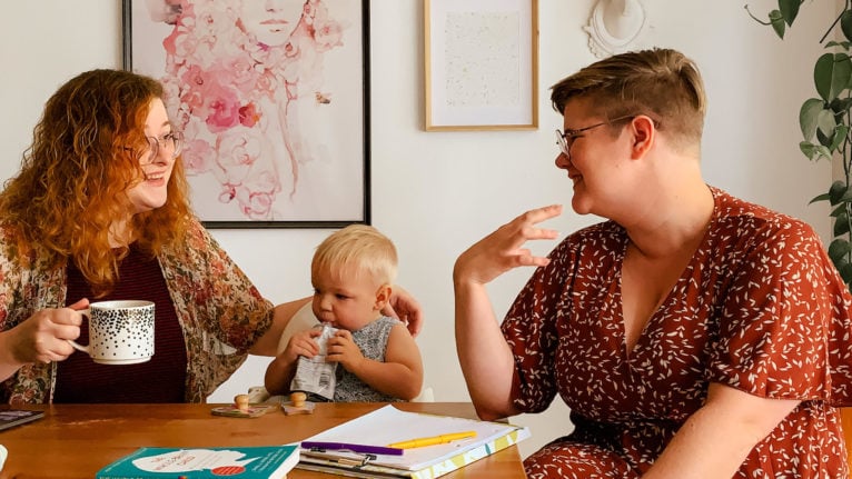 two women sit at a kitchen table with a toddler