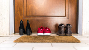 Three pairs of shoes sitting outside in front of a front door for a piece on whether to wear shoes inside