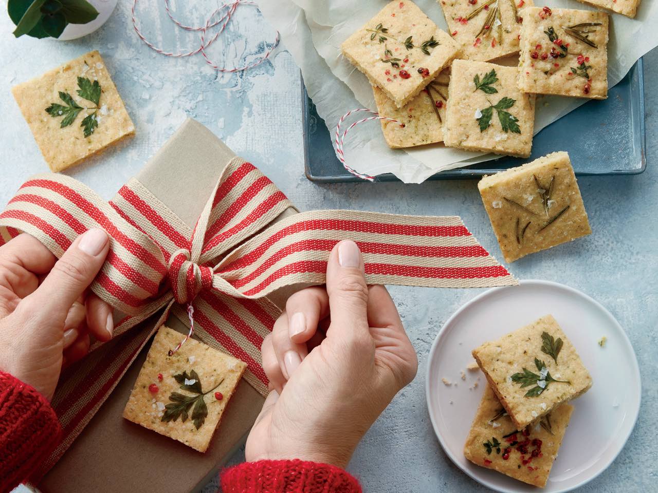 Savoury shortbread cookies on plate, next to brown-paper-wrapped gift with hands tying ribbon