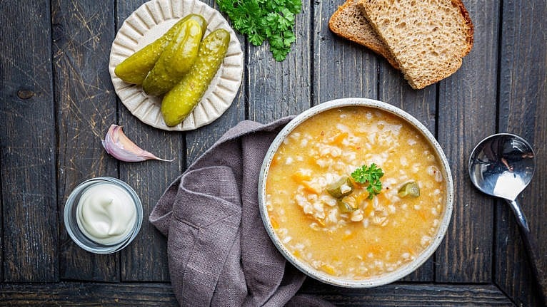 Soup with pickled cucumbers and pearl barley - rassolnik on wooden background, top view