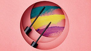Pink background with colourful mascara swipes and two black mascara wands, how to stop mascara from smudging
