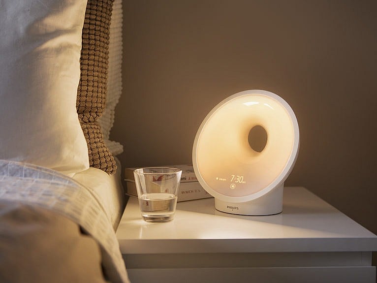 Wake-up light on white side table to the right of a bed.