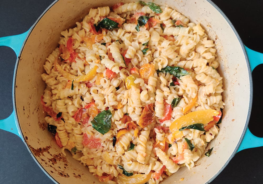 Cooked pasta with peppers, spinach, tomatoes and sausage in a pot.