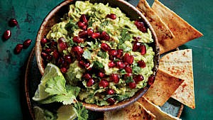 Pomegranate guacamole in brown bowl with tortilla chips on the side