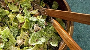A bowl of classic caesar salad, with salad tongs and croutons