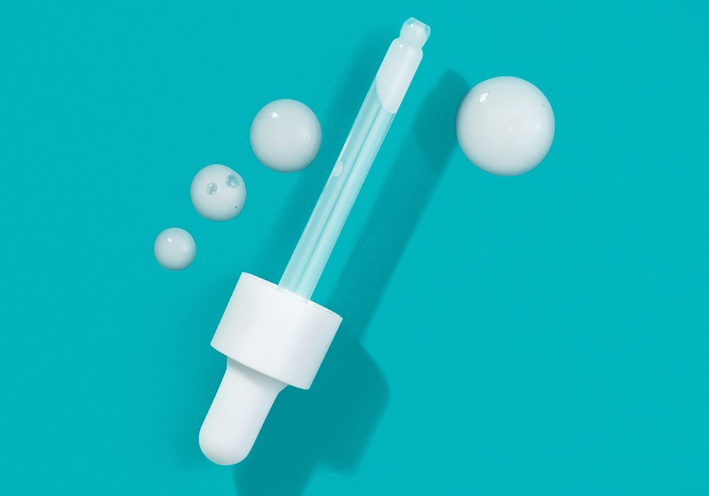 A dropper with serum on a turquoise background illustrating an article about how to use niacinamide skincare