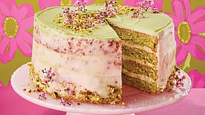 Pistachio cake with orange blossom icing on a pink plate infront of a floral backdrop