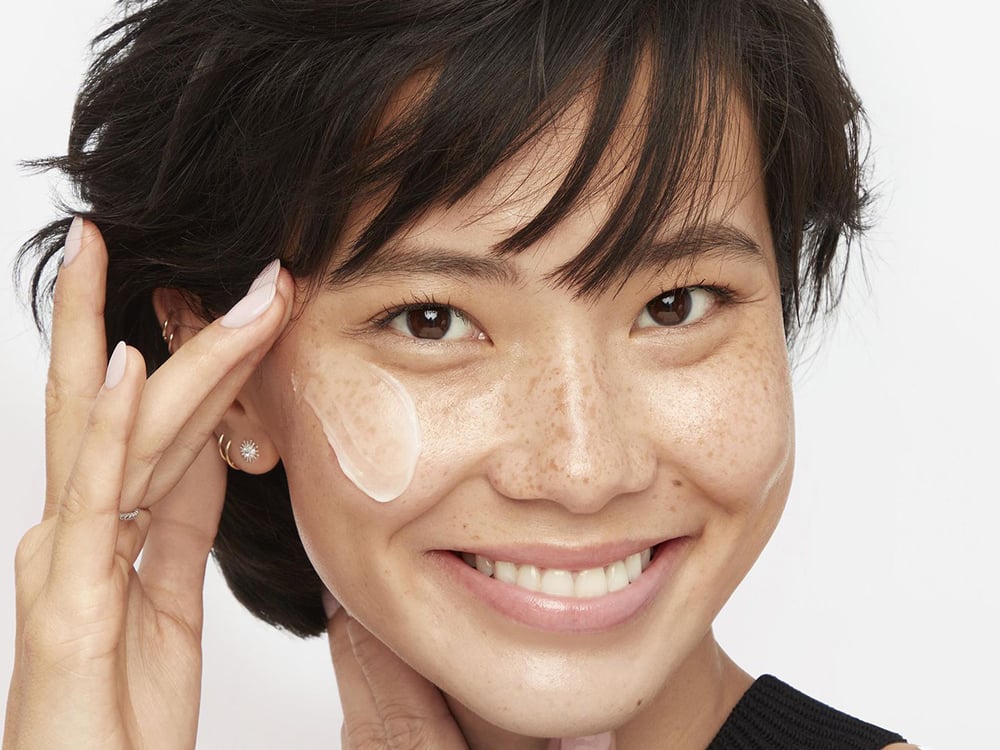 A woman applying face cream for an article on peptides as a skincare ingredient.