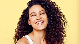 A model with curly hair against a yellow background to illustrate tips on how to air-dry hair.