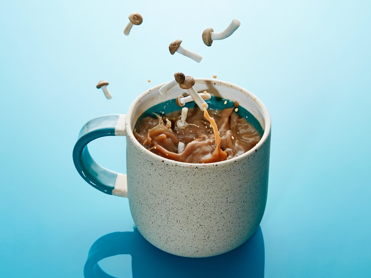 Mushrooms dropping into a mug of water against a blue background