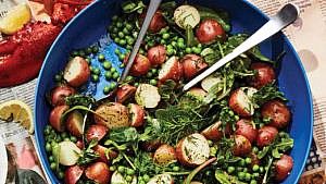 A bowl of potato salad with peas, fresh dill and leafy greens in a blue serving bowl.