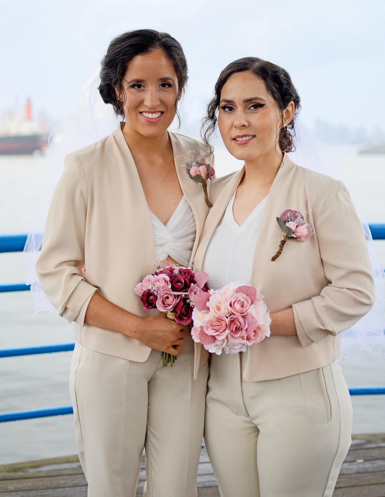 A newlywed female couple both with dark hair, both wearing cream suits