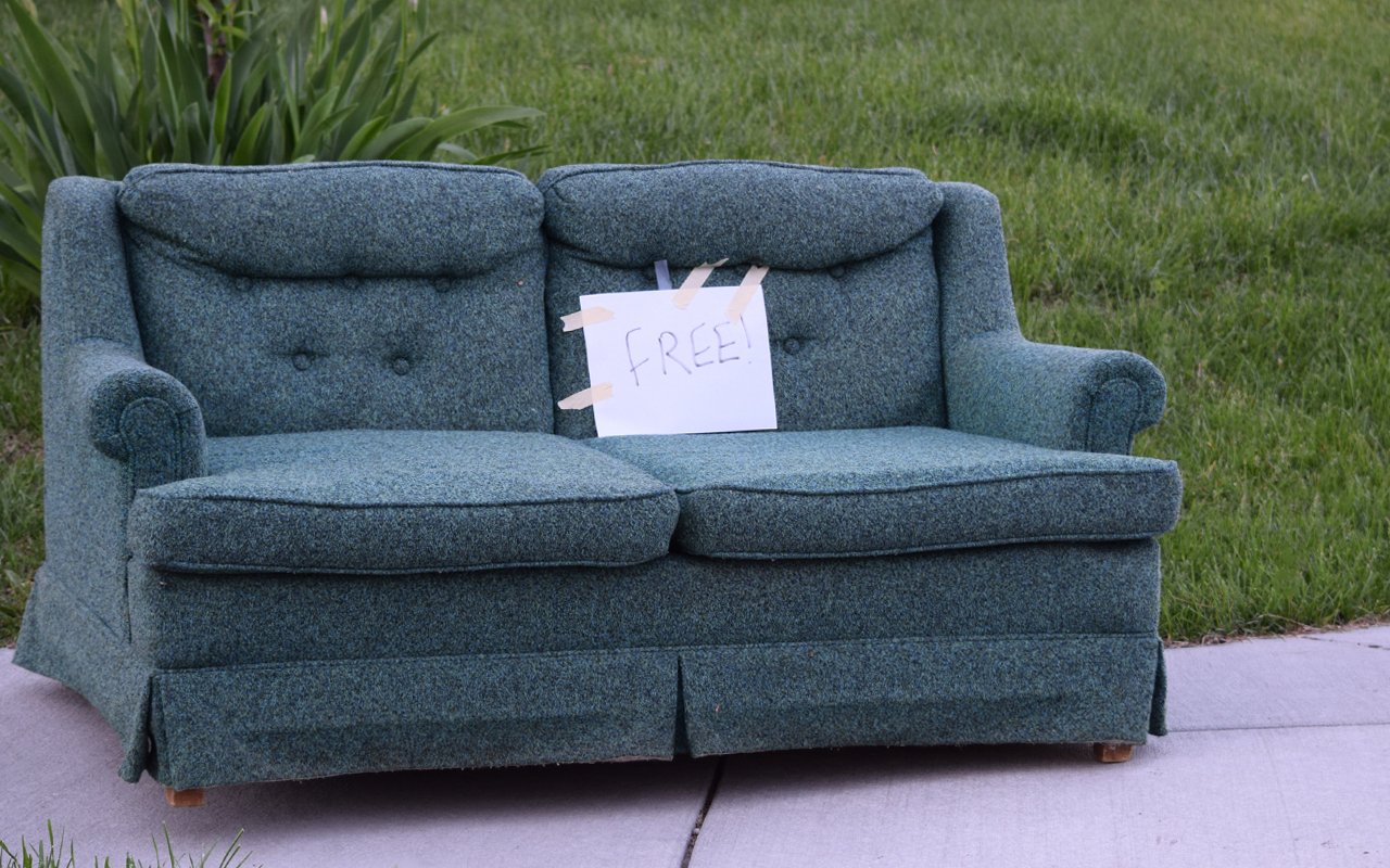 A teal couch with a sign marked "free" to illustrate an article on curbing and how to furnish your home for free.