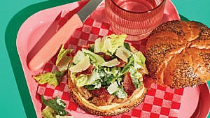 A chicken burger topped with romaine lettuce, bacon and caesar dressing
