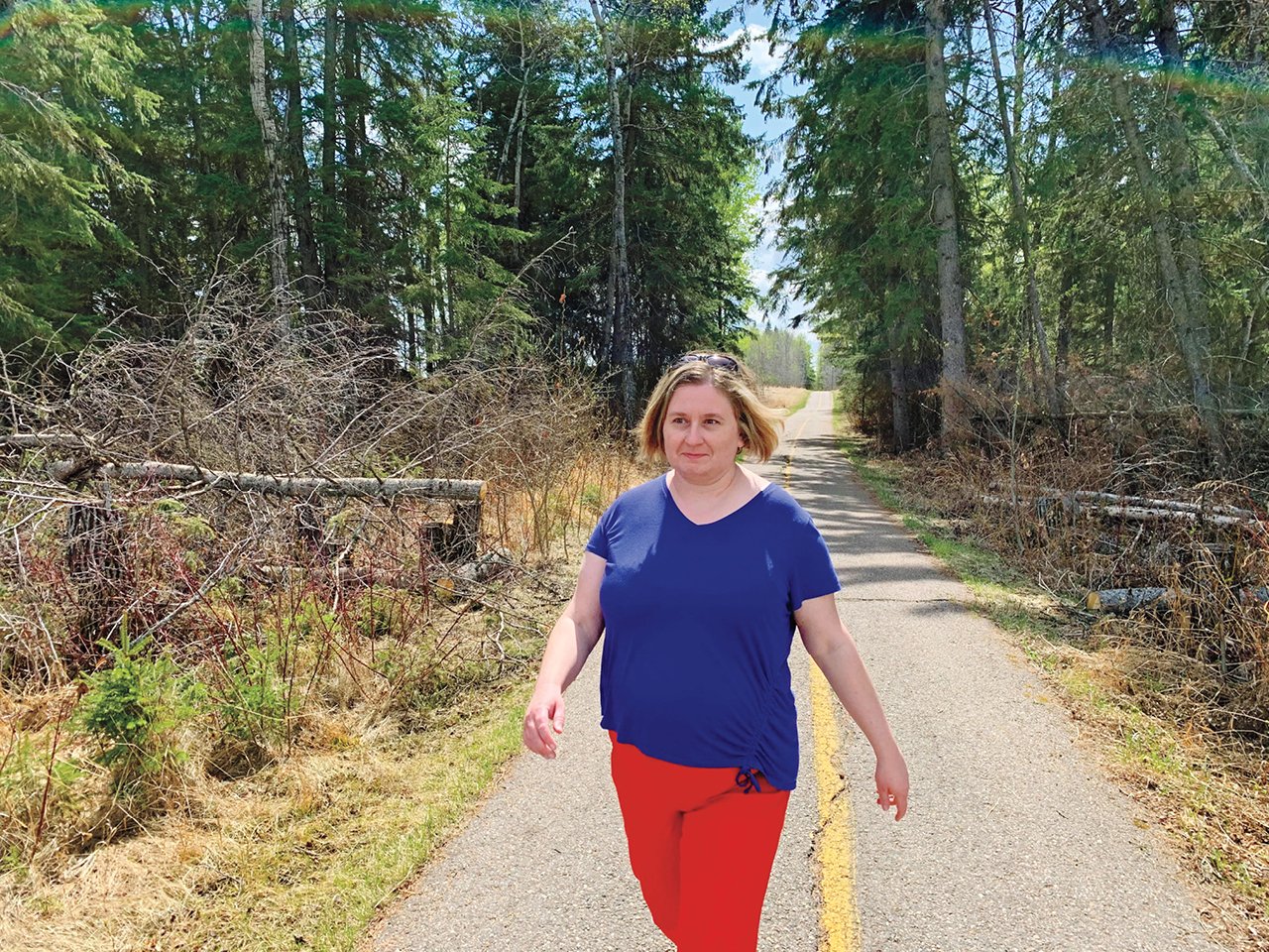 A woman in an indigo t-shirt and red pants walking down a road