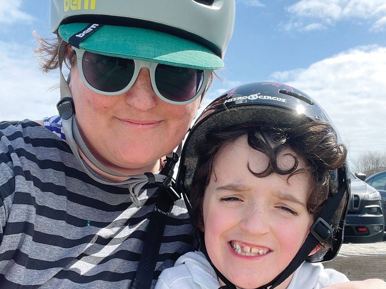 A selfie of the author and her son in bike helmets against a cloudy blue sky