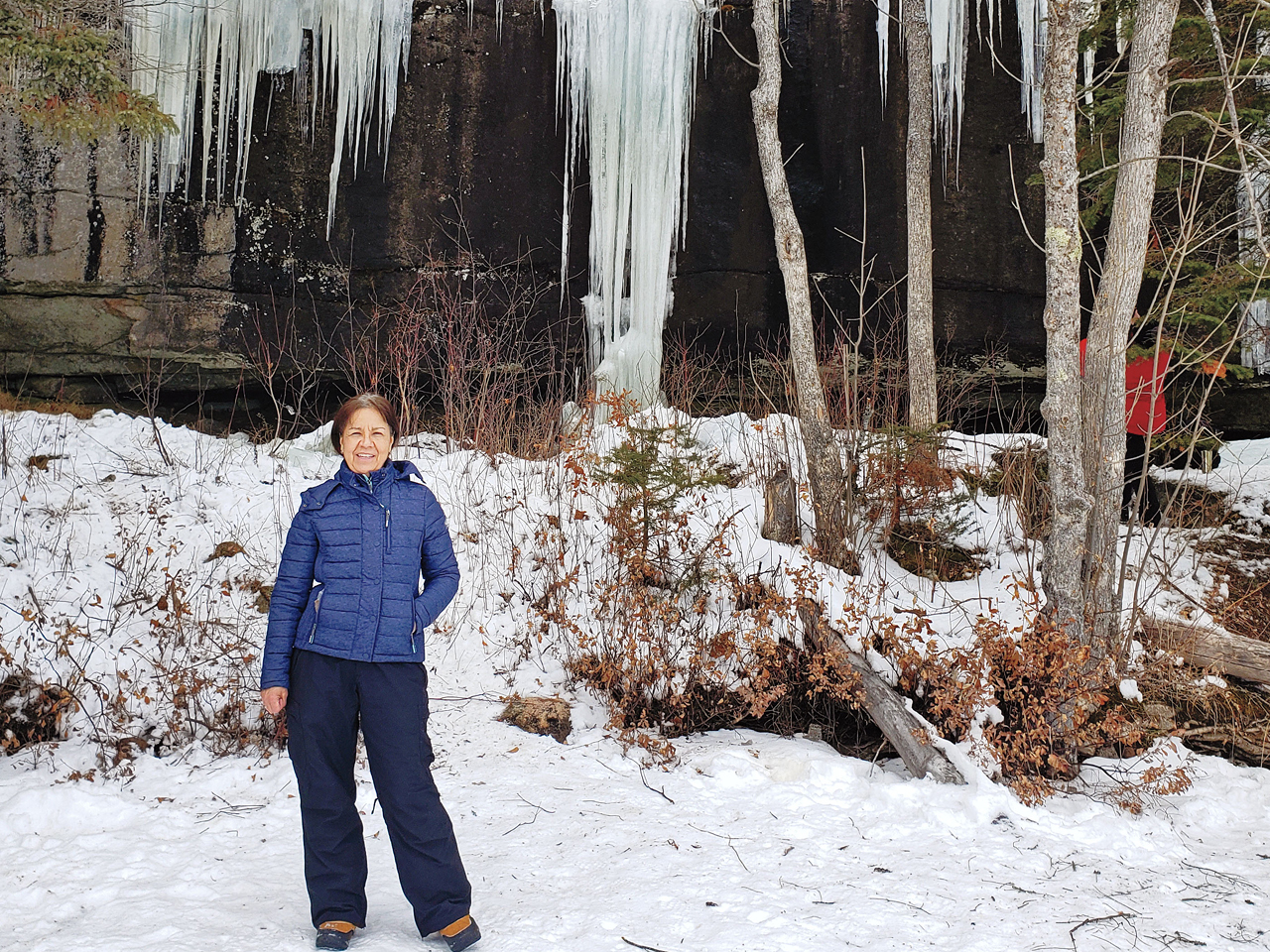 The author stands in front of the long icicles of a frozen waterfall