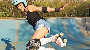 A woman in helmet, elbow, wrist, ankle and knee pads grabbing some air in her roller skates