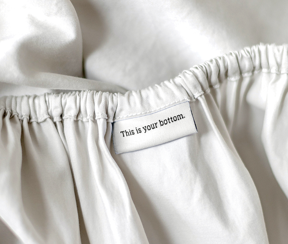 White bed sheet from Tuck with a tag that says "this is your bottom."