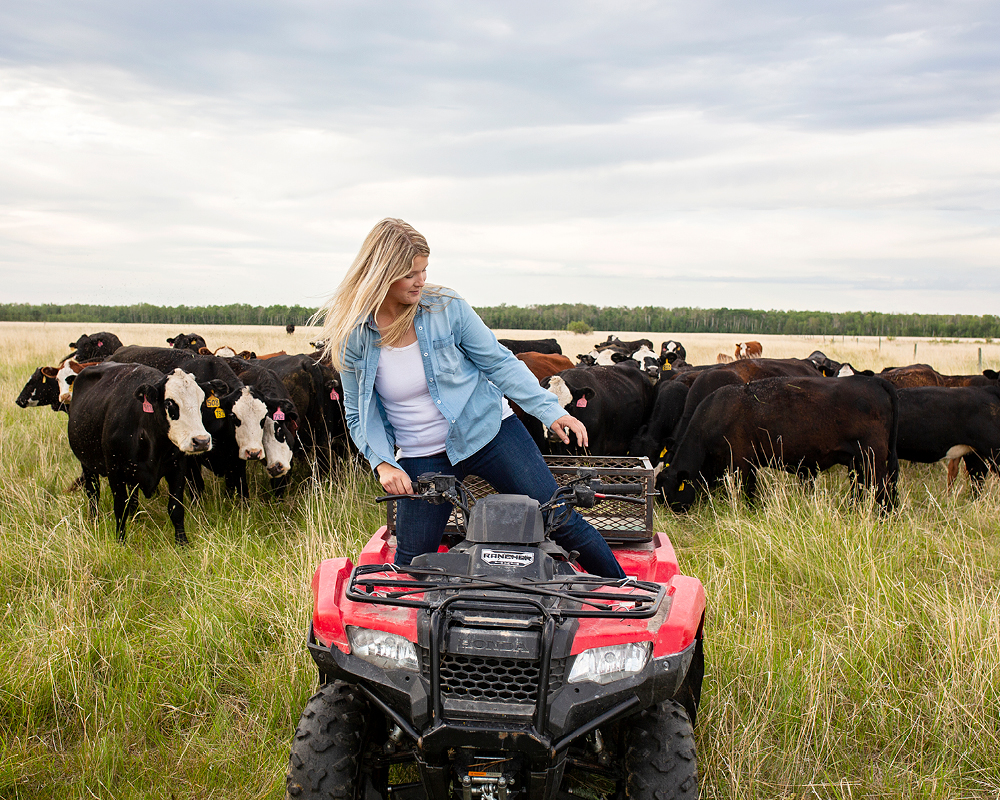Kristine Tapley poses on an ATV, with a group of grown cows behind her