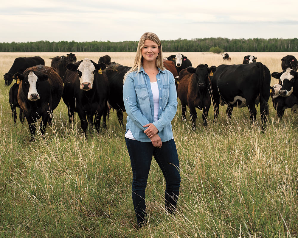 Kristine Tapley stands in grass, with a group of brown cows behind her