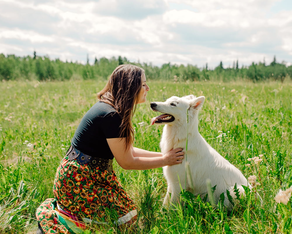 Tiffany Traverse sits in a field and faces a white dog that sits next to her