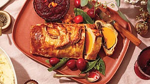 A vegetarian Thanksgiving butternut squash wellington, sliced, on a platter with cranberries