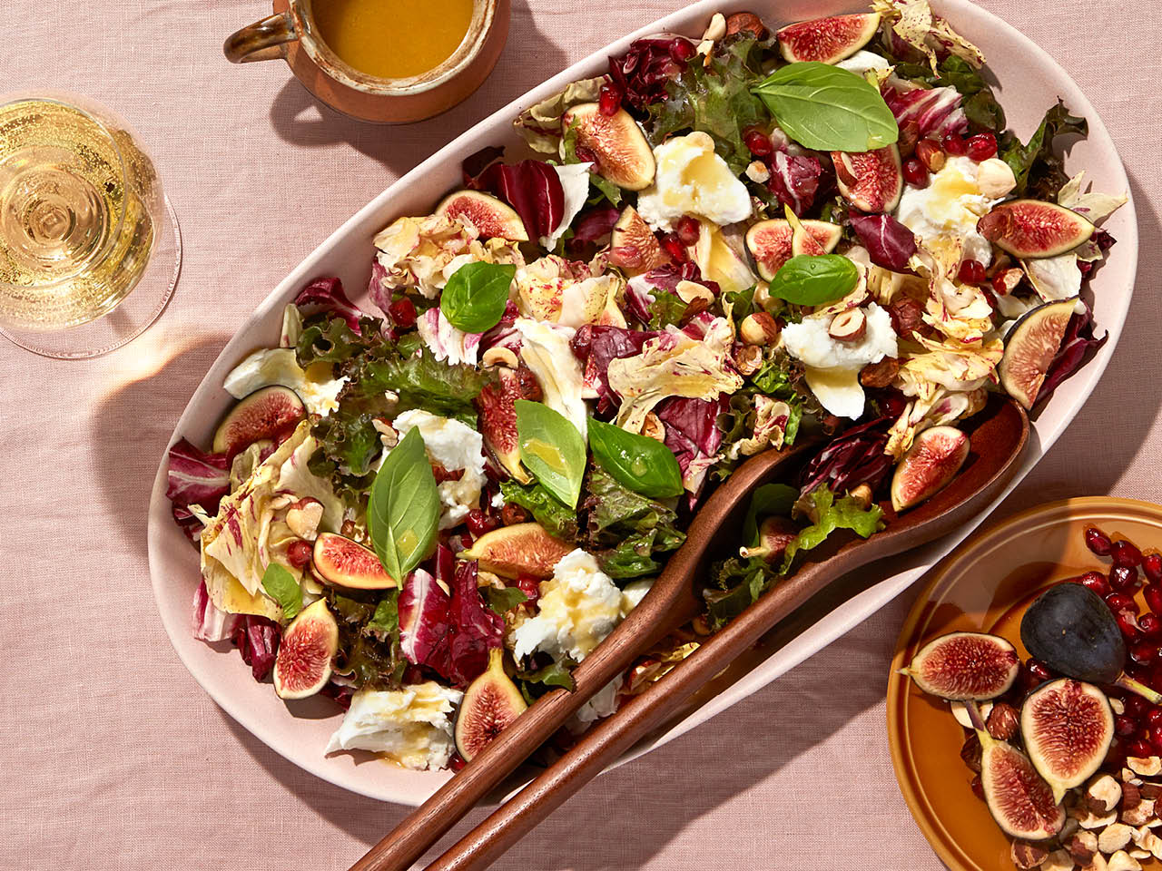 A bowl of fig and radicchio salad, set on a table with a sparkling beverage and a bowl of figs