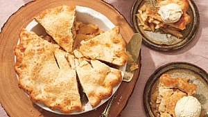 An apple pie with two slices cut out of it on a serving tray next to two plates of apple pie slices a la mode