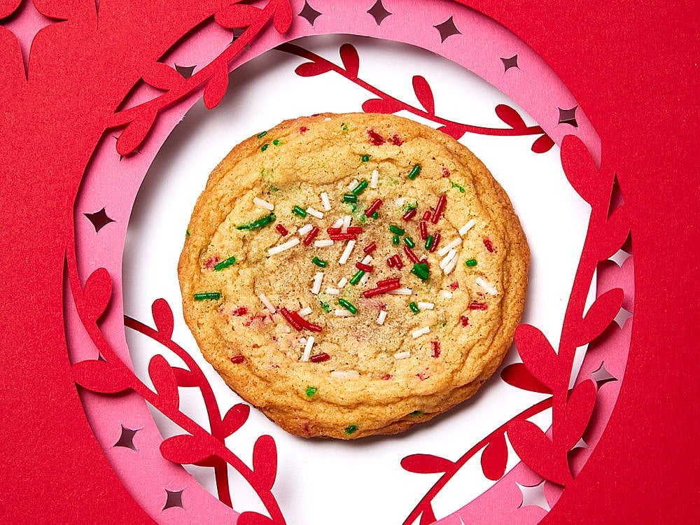 a brown butter holiday confetti cookie with red and green sprinkles in the centre of a cut-out paper ornament