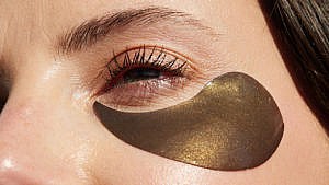 A woman wearing a glittery bronze eye patch, the best skincare patches for every concern
