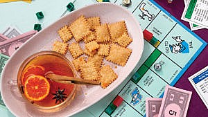 A pink plate with cheddar cheese crackers and a cup of mulled white wine with a star anise, sliced orange and cinnamon stick garnish