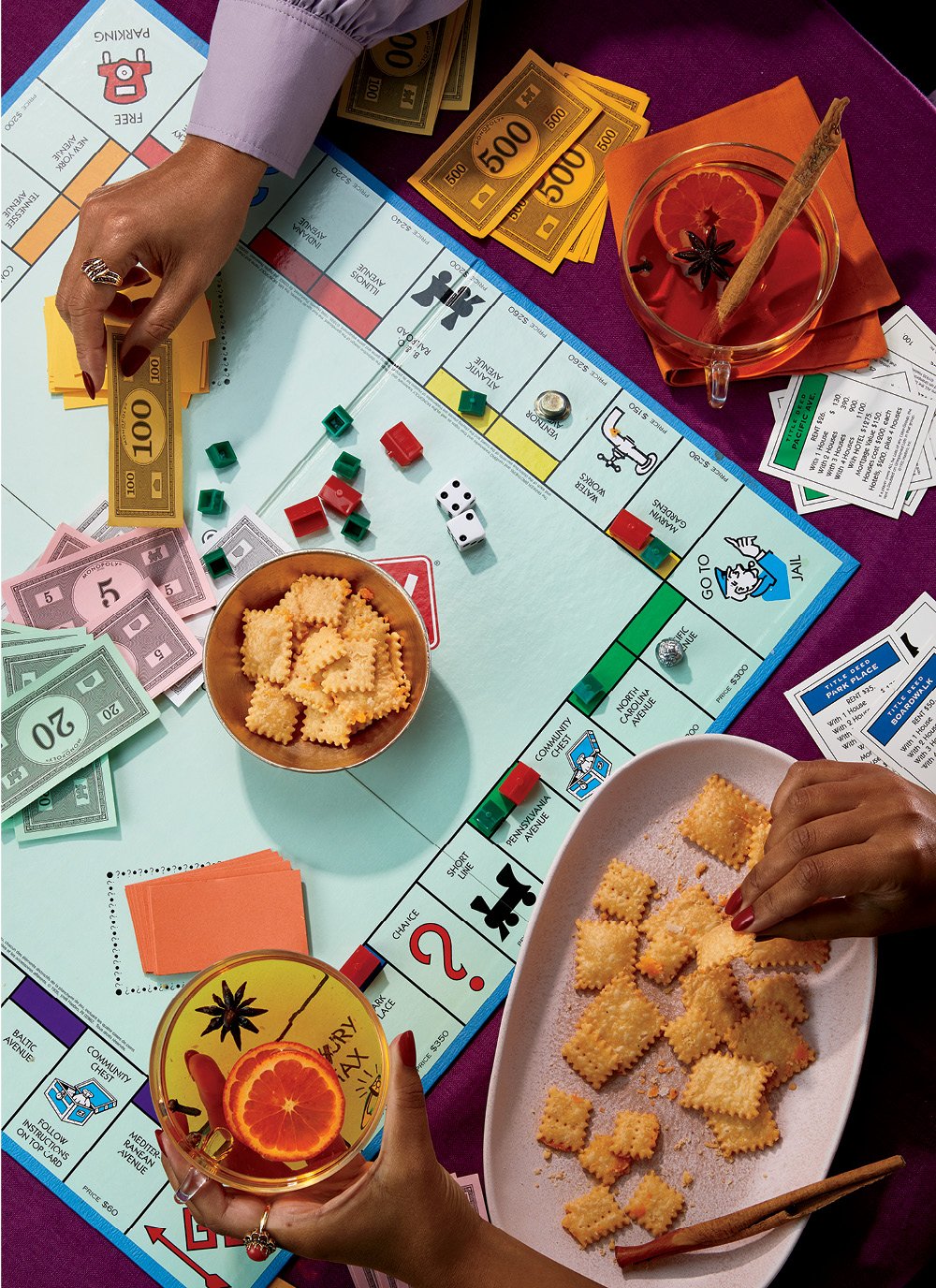 Cheddar Cheese Crackers with Mulled White Wine on a table with a burgundy tablecloth and two pairs of hands playing monopoly