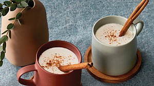 Two mugs with latte and cinnamon sticks inside