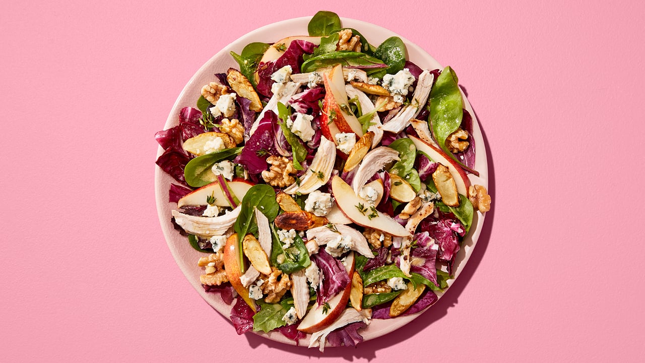 Leafy salad with pears, nuts and shredded chicken on a pink plate.