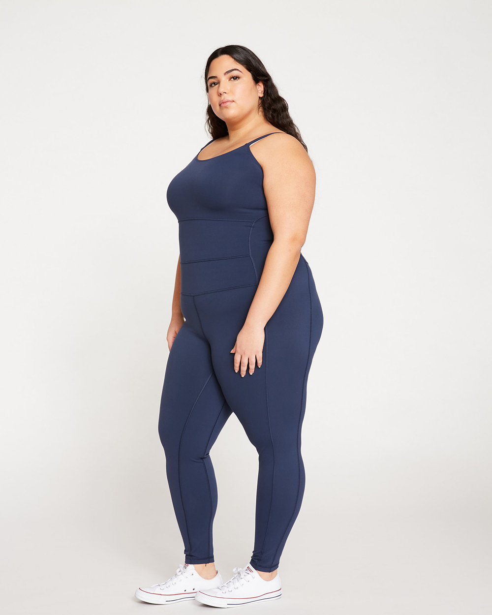 A model wearing a navy full-length workout bodysuit from Universal Standard and standing against a white background.